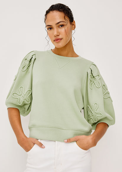 Woman wearing a light green tops with floral patterns on a white background