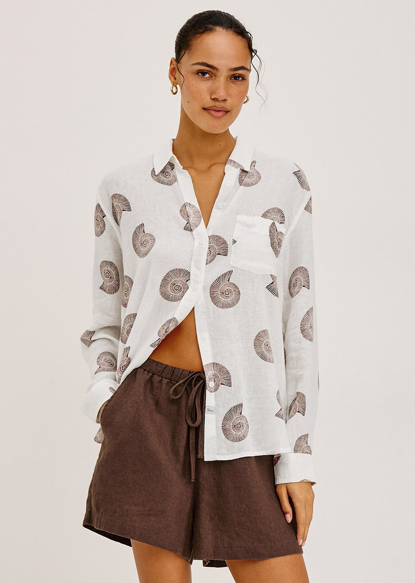 Woman wearing a white shirt with brown seashells and brown shorts