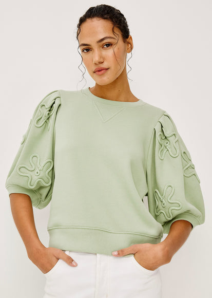 Woman wearing a light green top with decorative sleeves against a white background