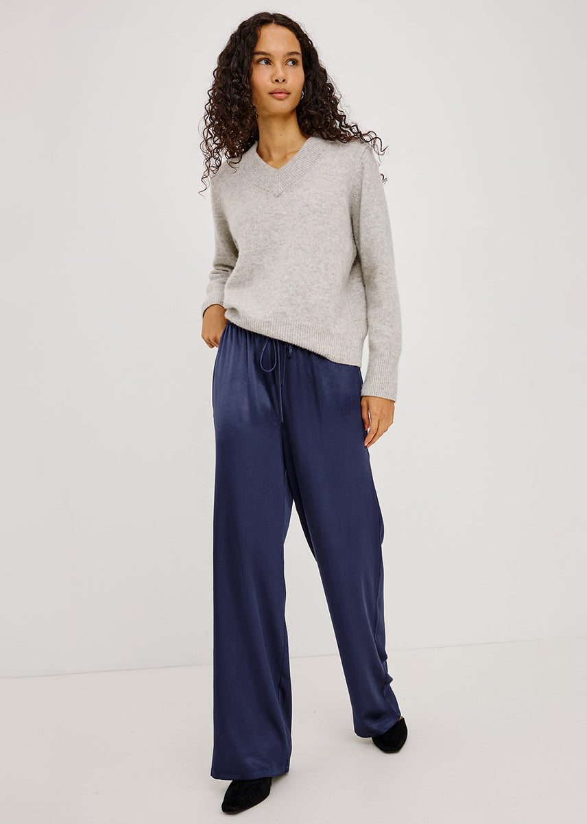 A woman modeling a light gray knit sweater and navy wide-leg satin pants against a plain white studio background.