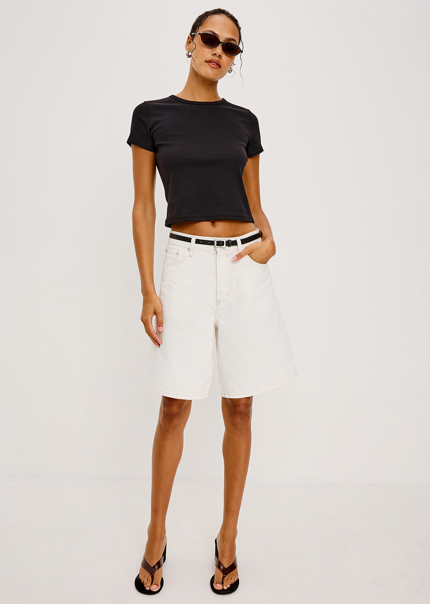 Woman wearing a black crop top and white shorts on a plain background