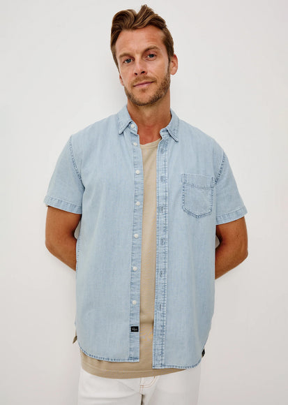 Man wearing a light blue denim shirt over a beige t-shirt on a white background
