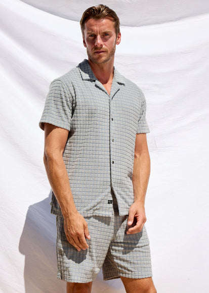 Man wearing a checkered shirt and shorts set against a white background