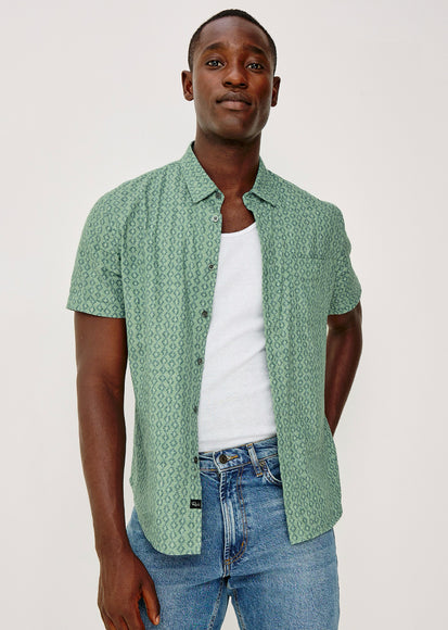 Man wearing a green patterned shirt over a white t-shirt and blue jeans on a white background