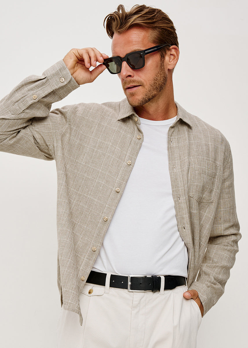 Man wearing a beige shirt and light bottoms against a white background