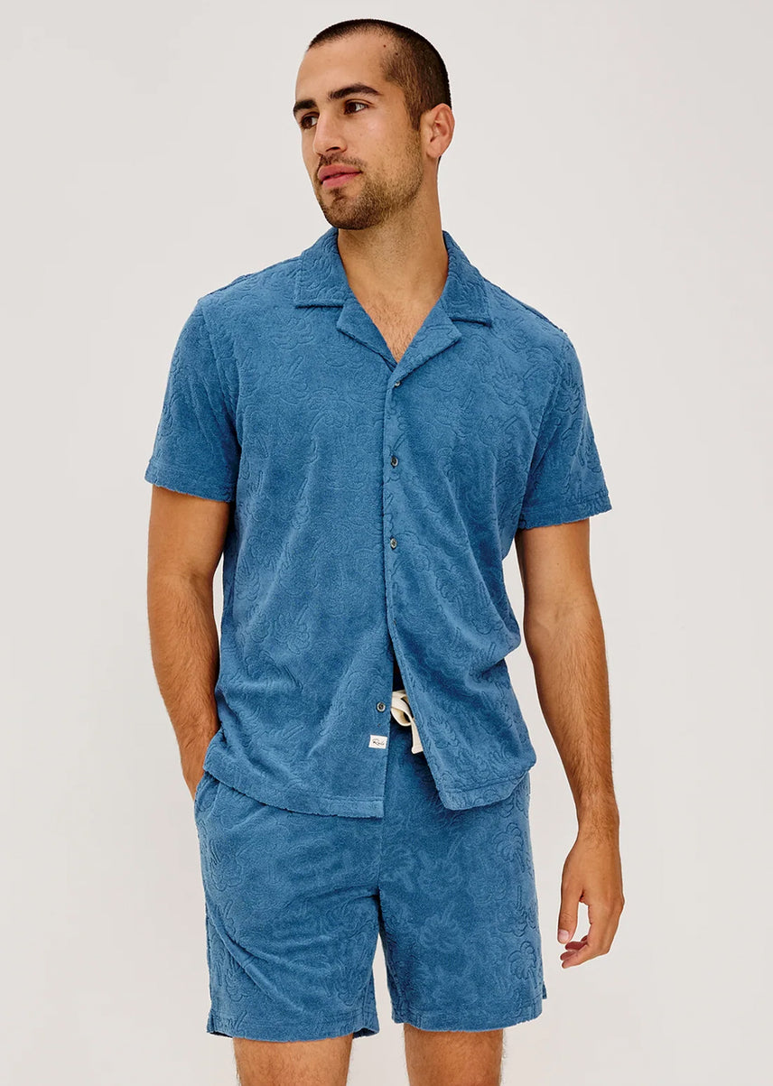 Man wearing a blue textured shirt and shorts set against a plain background