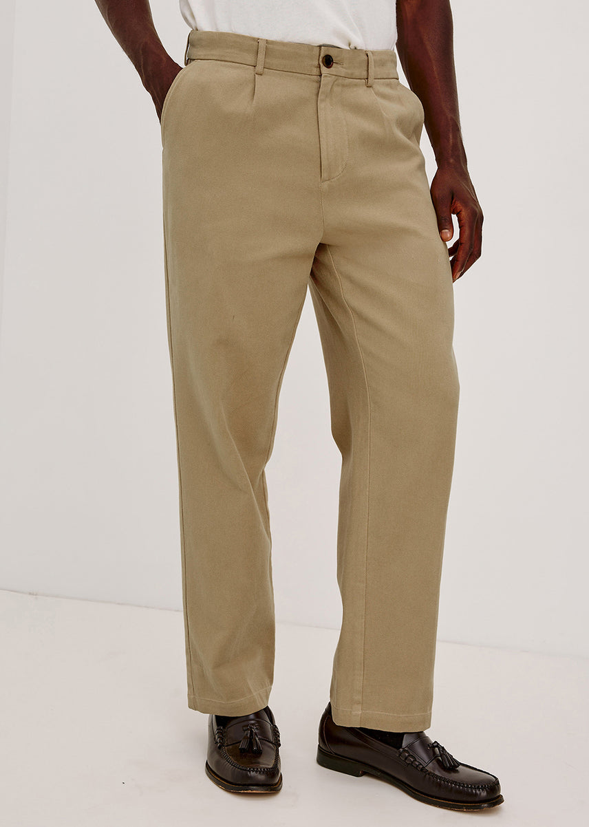 Man wearing a beige pair of pants with brown loafers against a white backgrond
