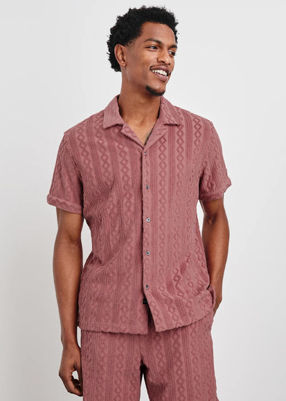 Man wearing a patterned pink shirt and shorts on a white background