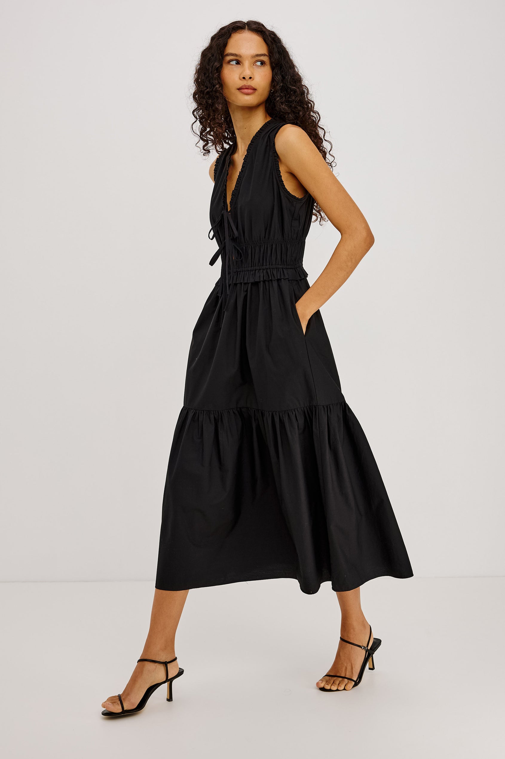 Dana Midi Dress in Cotton Poplin With Deep V-Neck and Center-Front Ties, Laddered Elastic Waist, Fully Lined Tiered Skirt, On-Seam Side Pockets, and Ruffle Trim in Black Colorway - Full Body Side View Featured on Model