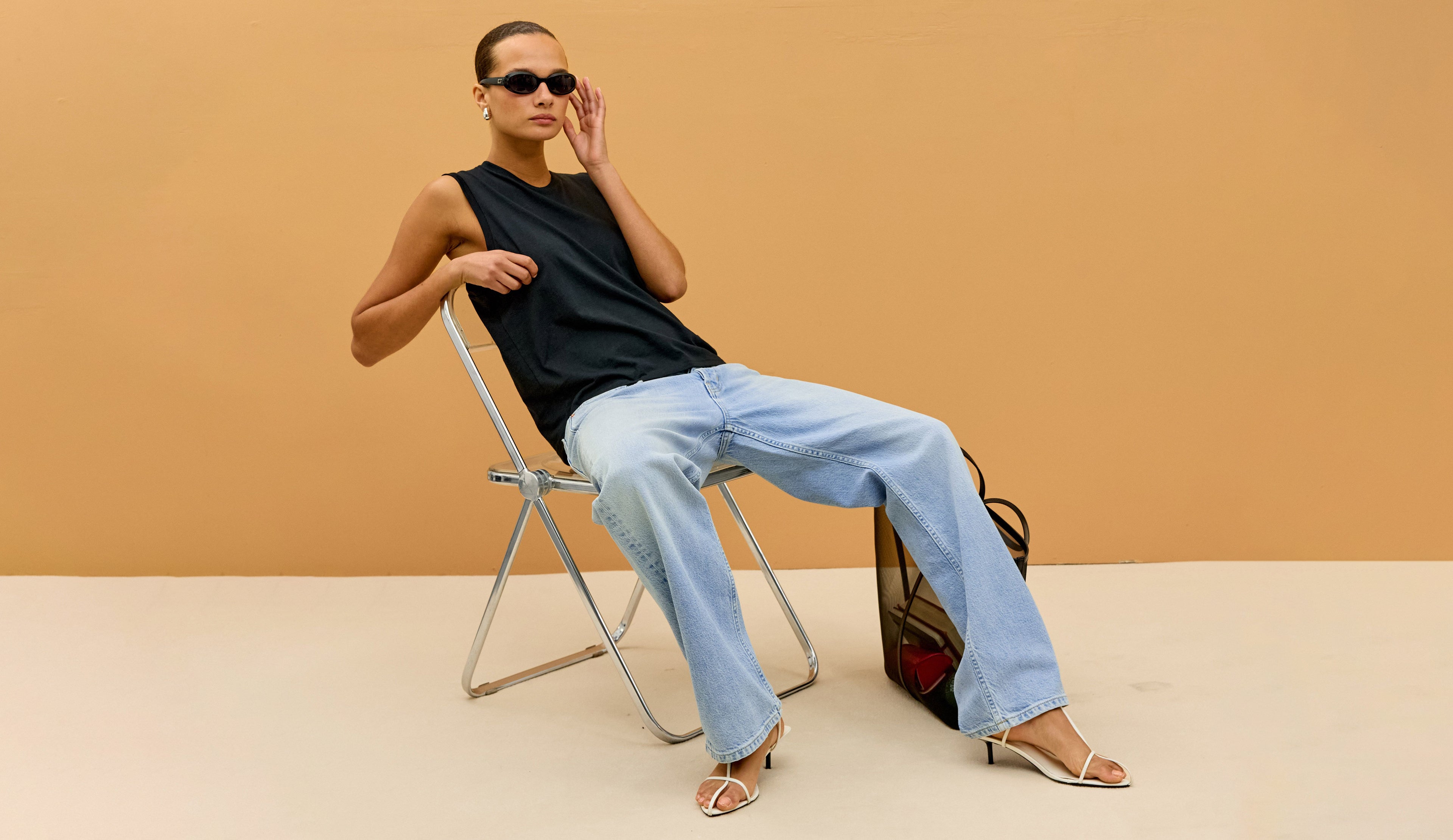 Woman sitting on a chair against a beige wall with a bag next to her.