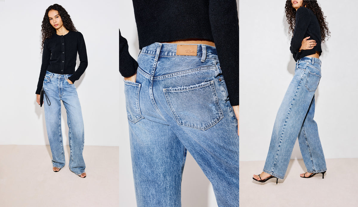 A woman modeling a pair of wide-leg light blue denim jeans with a black cropped long-sleeve top and black strappy heels, standing against a plain off-white studio background.