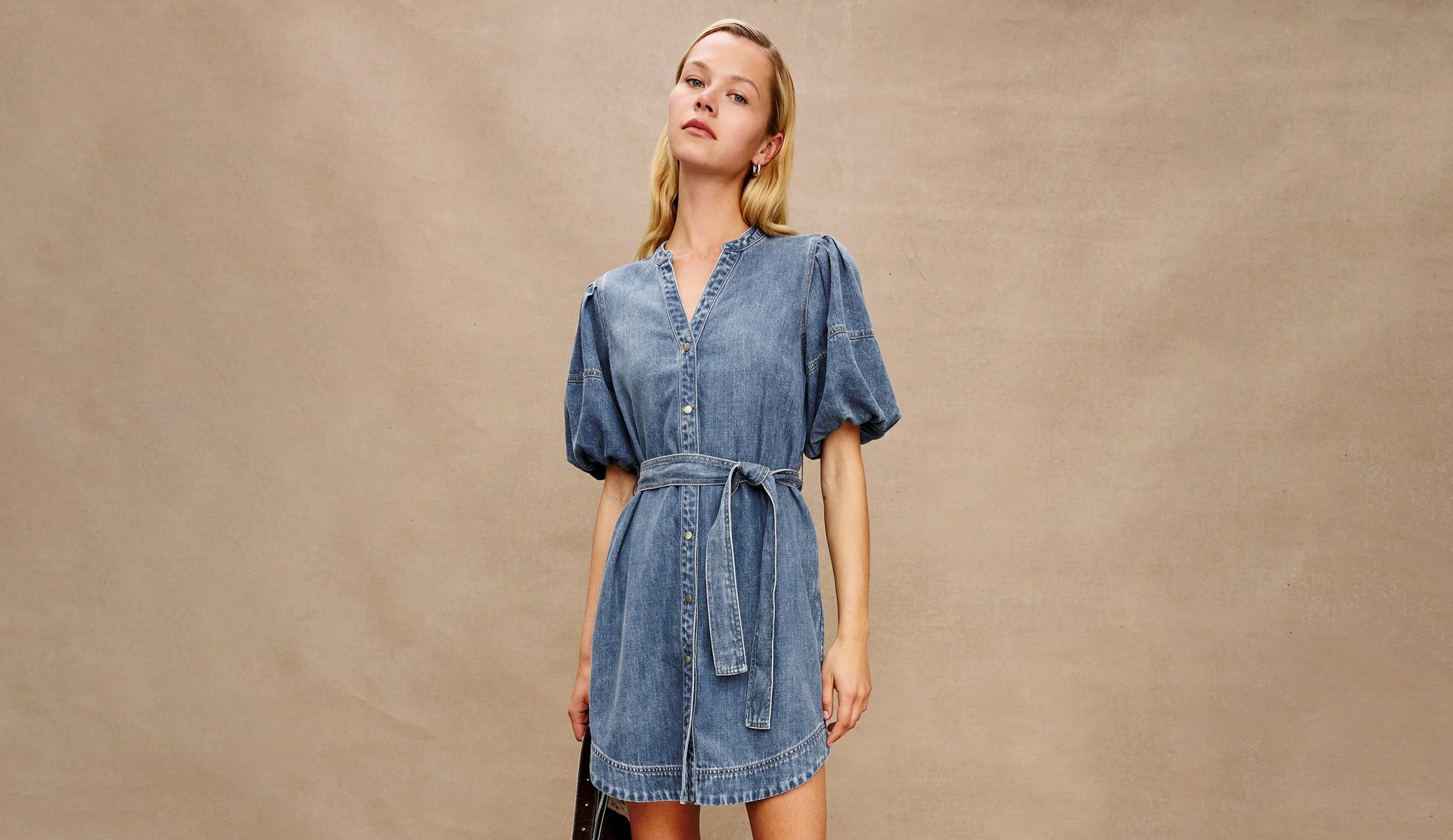 Woman wearing a denim dress against a beige background