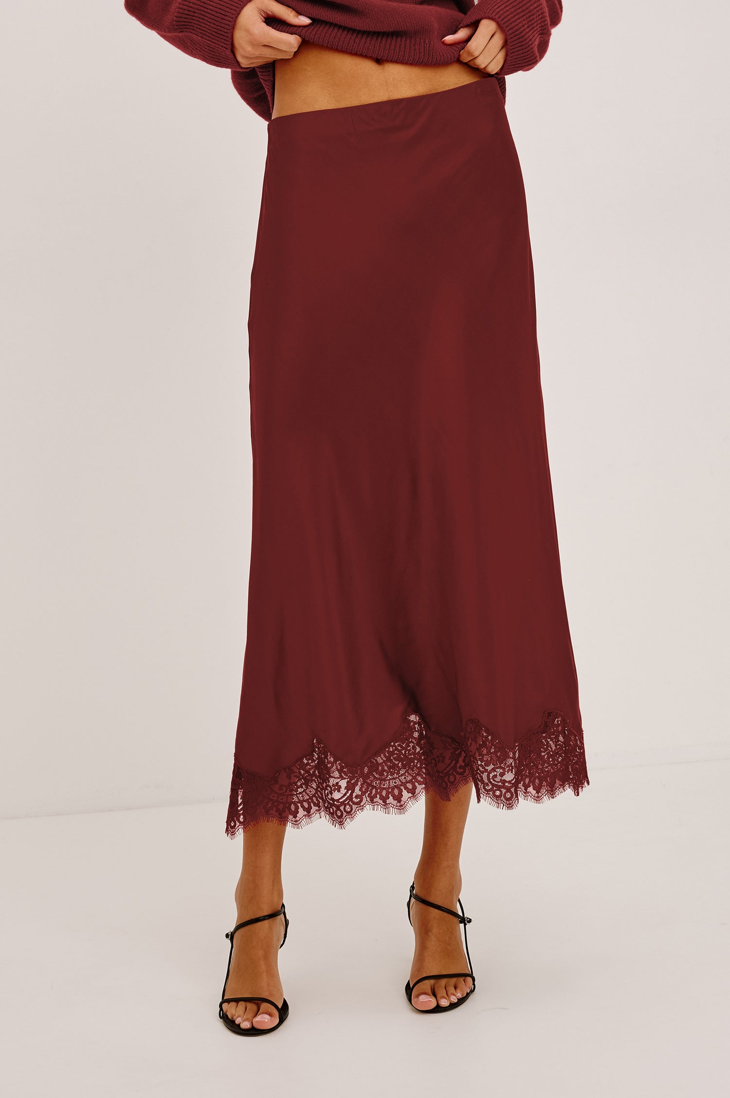 Ebony Midi Skirt Bias Cut in Satin With Clean Elastic Waistband, Pull-On Fit, and Tonal Lace Trim at Hem in Crimson Colorway - Lower Body Front View Featured on Model