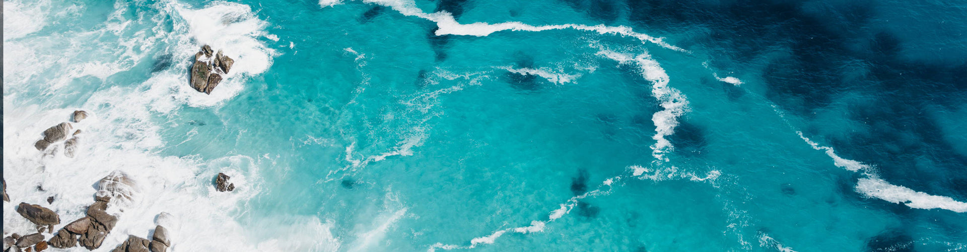 OVERHEAD SHOT OF THE OCEAN TAKEN FROM ABOVE AND LOOKING DOWN AT LIGHT BLUE WATER AND ROCKS