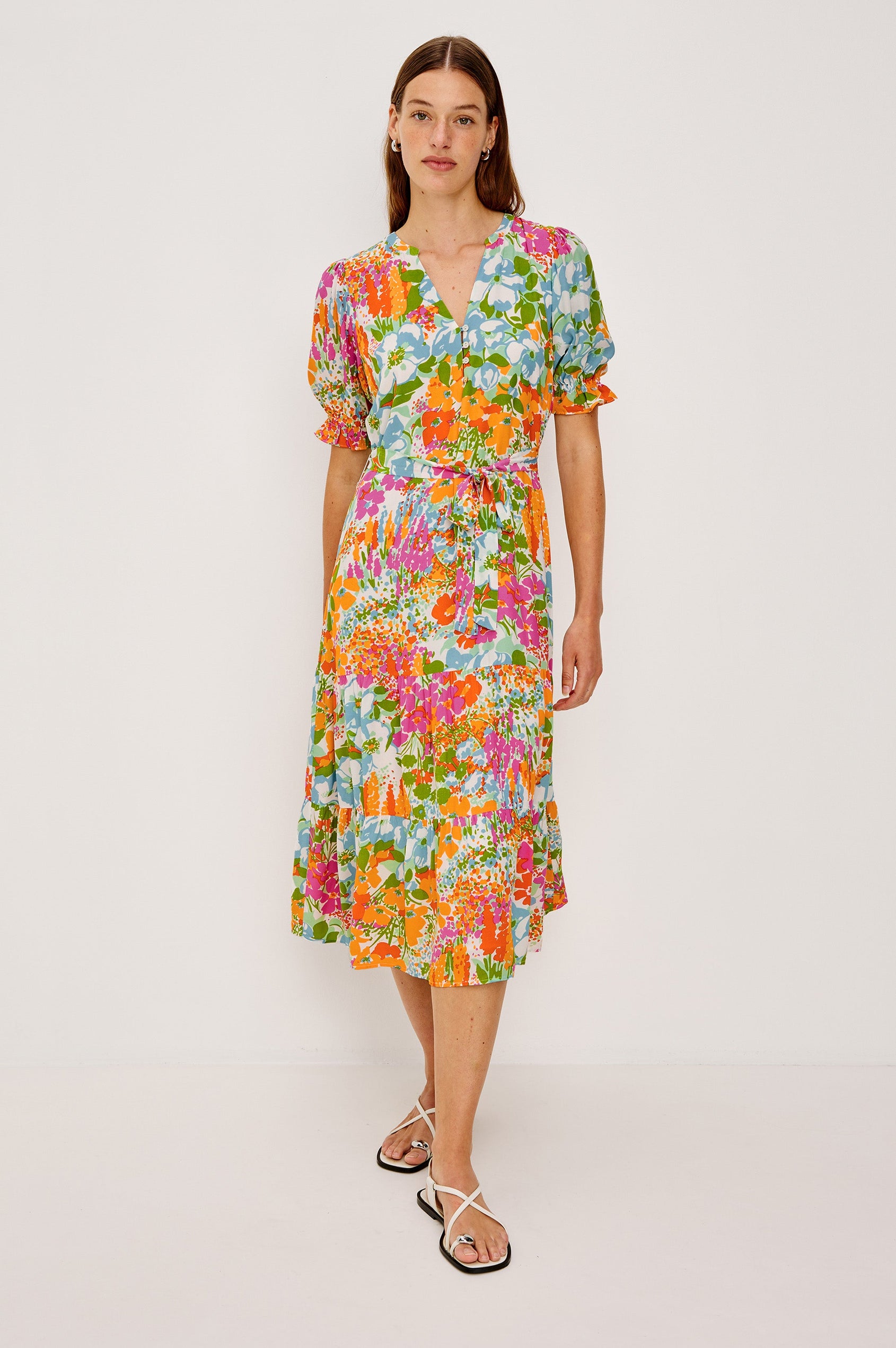 Eliana Midi Dress with Elbow-Length Sleeves with Shirred Cuffs, a V Neck, Buttons Down the Bodice, a Fabric Tie at the Waist  and a Tiered Skirt in Day Garden Colorway, a Floral Pattern in Blue, Pink and Oranges on White - Front Full Body View Featured on Model