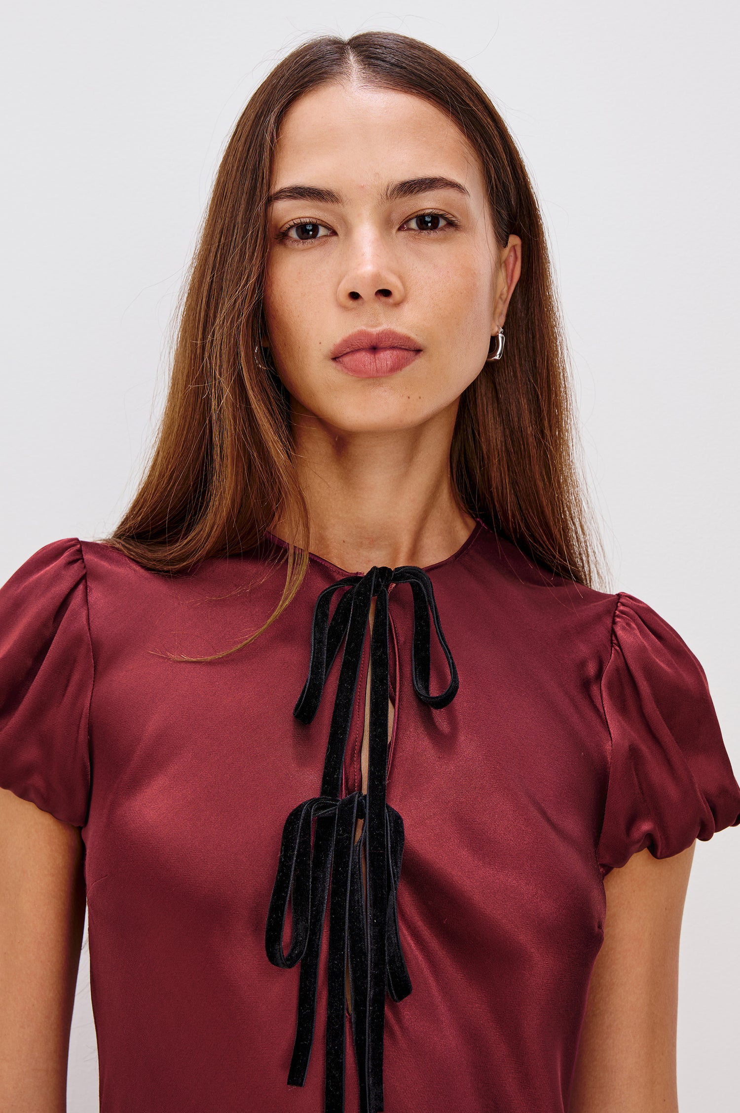 Elyssa Mini Dress in Satin Back Crepe With Bias Cut, Short Puff Sleeves, and Deep V-Neckline With Velvet Bow Self-Ties in Garnet Colorway - Upper Body Close Up View Featured on Model