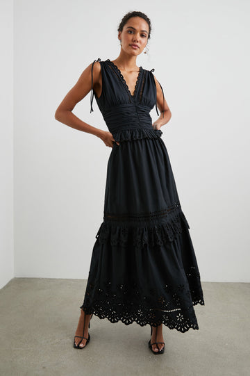 Esmeralda Sleeveless Maxi Dress with a Deep V Neck, a Ruched Waistband, Drawstrings Across the Shoulder Straps, Scalloped Trim with Cutouts on the Bodice, a Tiered Skirt, and an Eyelet Design along the Hem in Black Colorway - Front Full Body View Featured on Model 