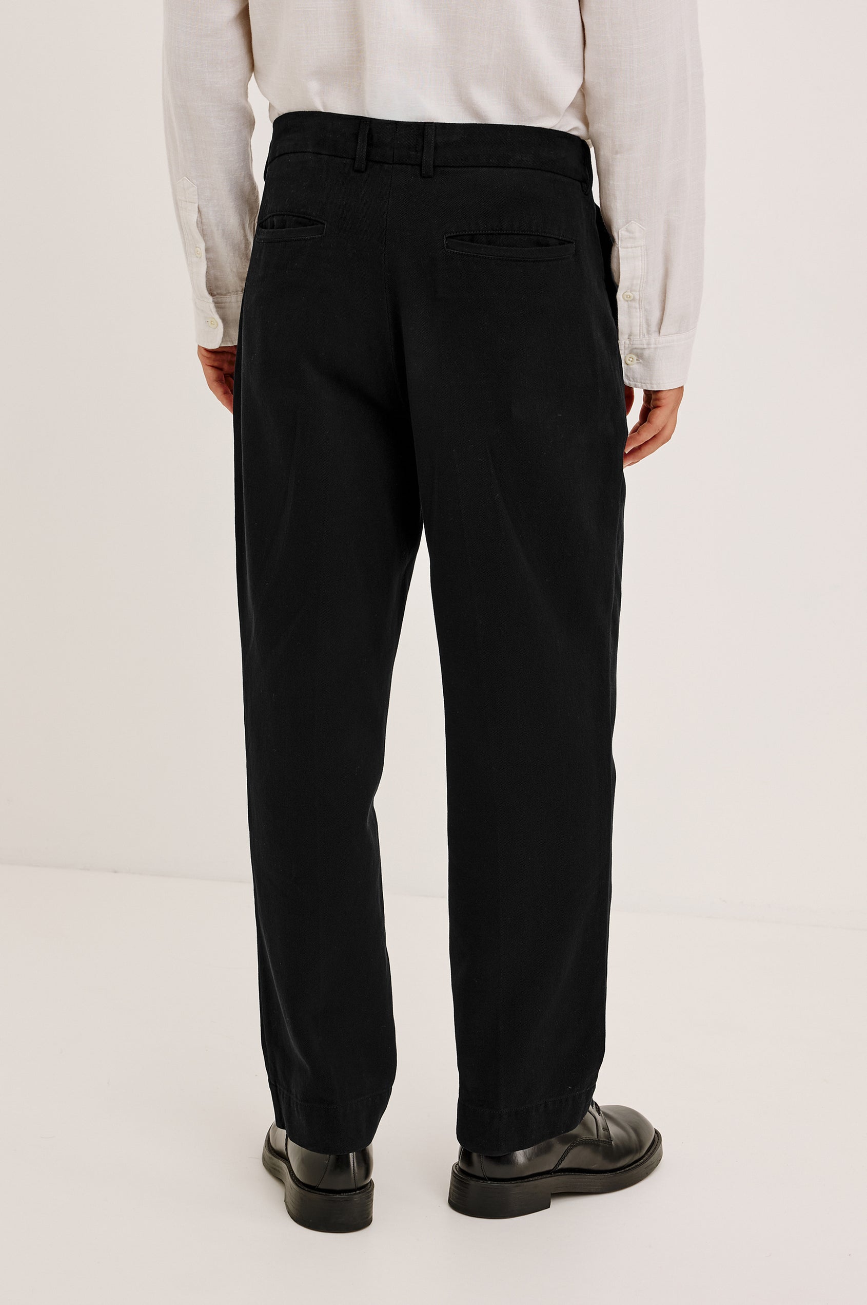Ezra Pant in Brushed Cotton Twill With Relaxed Fit, Single Front Pleats, Ankle-Length Hem, Zip Fly, Side Pockets, and Back Double-Welt Pockets in Black Colorway - Lower Body Back View Featured on Model