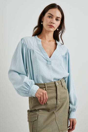 Fable Long Sleeve Top with a V Neck with a Placket, Buttoned Cuffs, and Pleating Down From the Yoke in Light Vintage Colorway, a Blue - Front Tucked View Featured on Model 