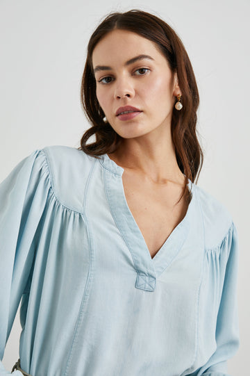 Fable Long Sleeve Top with a V Neck with a Placket, Buttoned Cuffs, and Pleating Down From the Yoke in Light Vintage Colorway, a Blue - Front Tucked View Featured on Model 