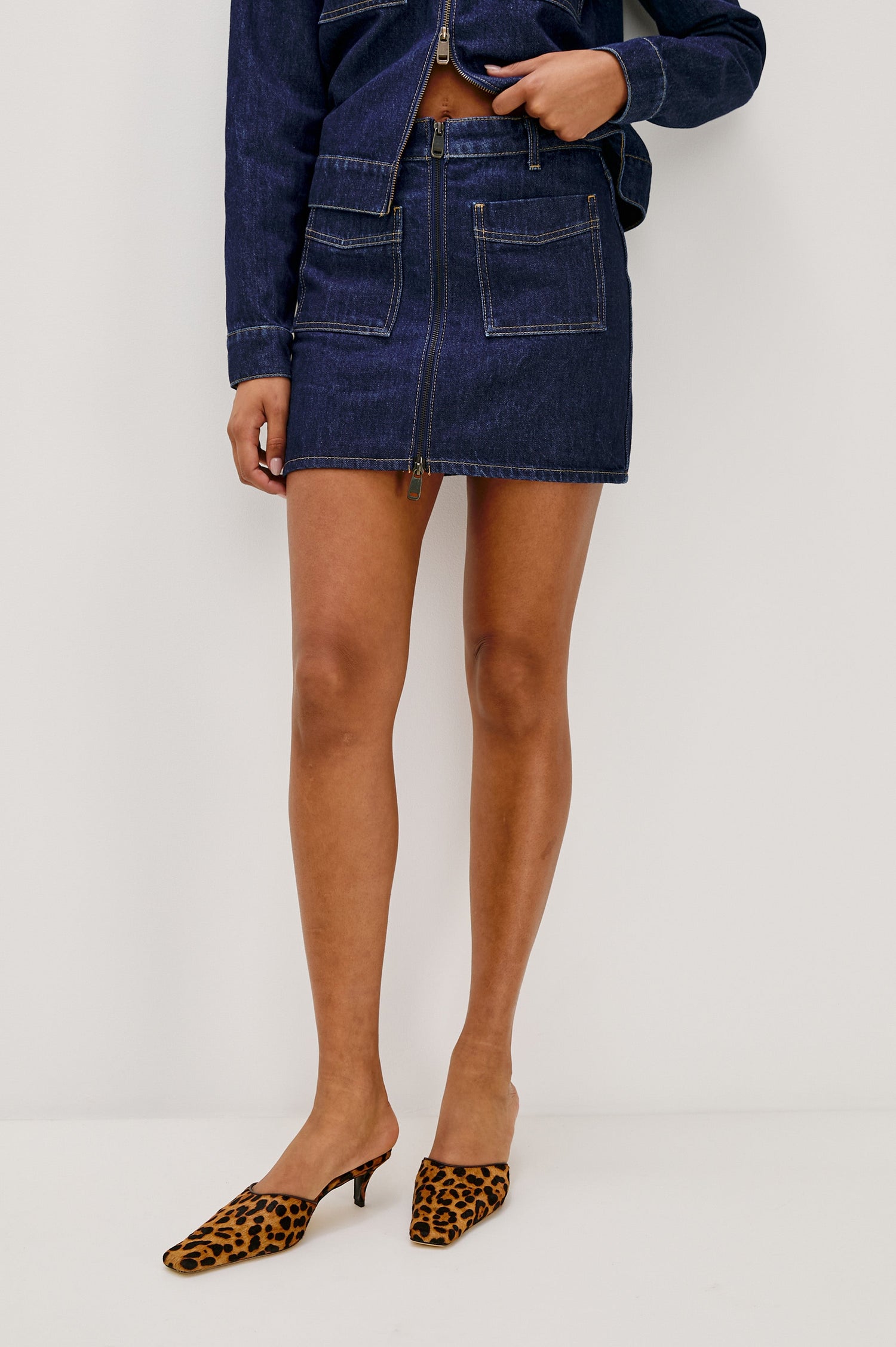 The Fallbrook is a mini zip front denim skirt with beltloops, front patch pockets and back pockets in Deep Indigo colorway. Front view featured on model.