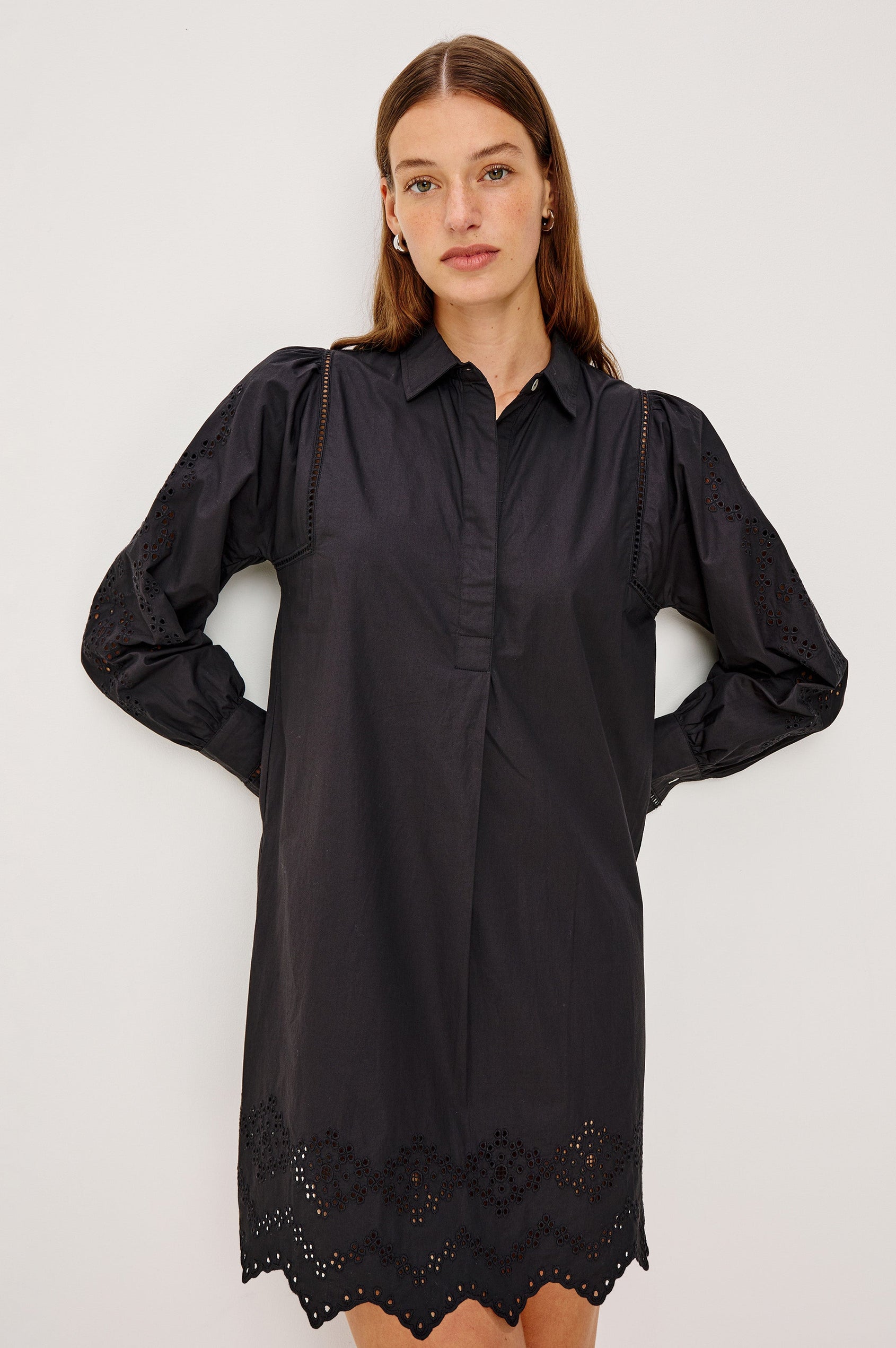 Fernanda Long-Sleeve Mini Dress with Button Cuffs, a Collar, a Placket with Buttons, a Scalloped Hem, a Floral Eyelet Design on the Sleeves and a Floral and Geometric Eyelet Design on the Hem in Black Eyelet Colorway - Front View Featured on Model