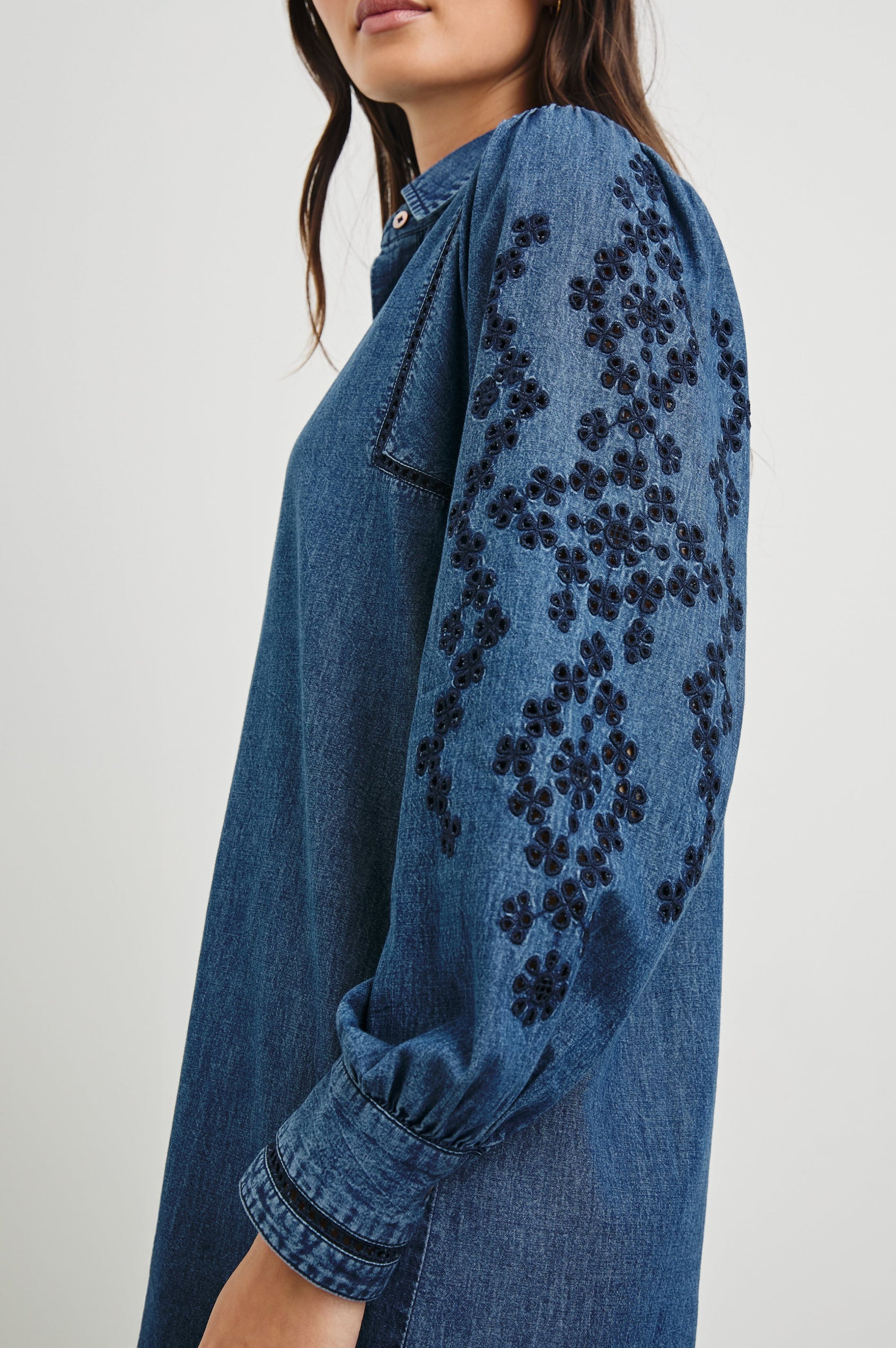 Fernanda Long-Sleeve Mini Dress with Button Cuffs, a Collar, a Placket with Buttons, a Scalloped Hem, a Floral Eyelet Design on the Sleeves and a Floral and Geometric Eyelet Design on the Hem in Dark Vintage Wash Colorway - Side View Featured on Model