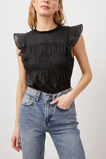 Filomena Short Sleeve Top with Flutter Sleeves, a Ruffled Neck, a Shirred Center Bodice, Lace Inserts and a Buttoned Keyhole at the Back in True Black Colorway - Front Tucked View Featured on Model