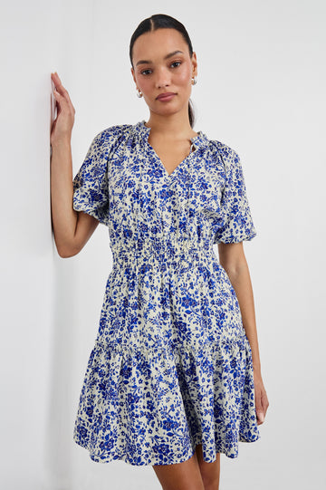 Fiorella Above-Knee Dress with Short Elasticated Puff Sleeves, Split V-Neck with Self Ties, and an Elasticated Ruched Waist Detail in Blue Marguerite Colorway. Front View Shown on Model.