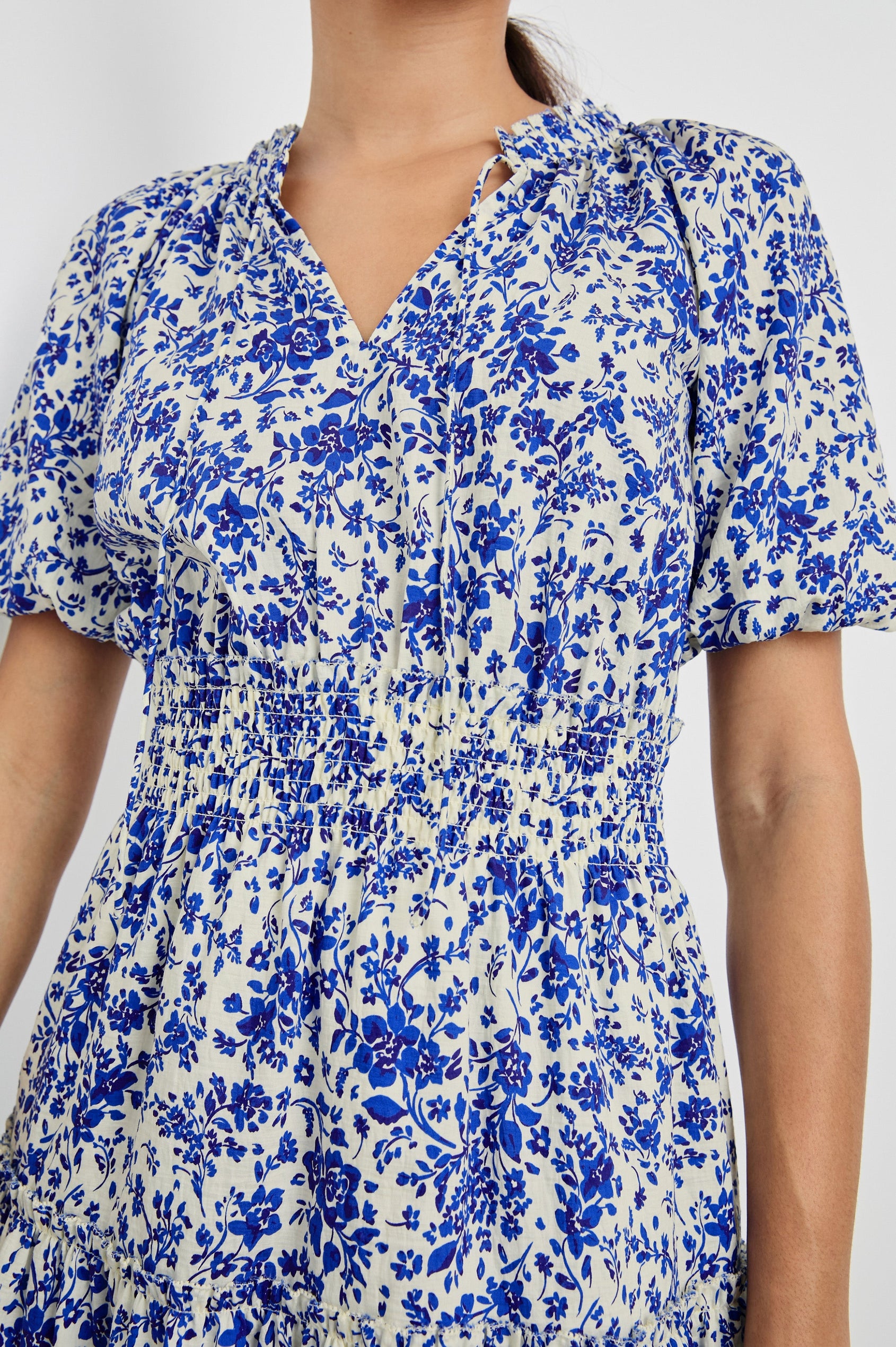 Fiorella Above-Knee Dress with Short Elasticated Puff Sleeves, Split V-Neck with Self Ties, and an Elasticated Ruched Waist Detail in Blue Marguerite Colorway. Front Detailed View Shown on Model.