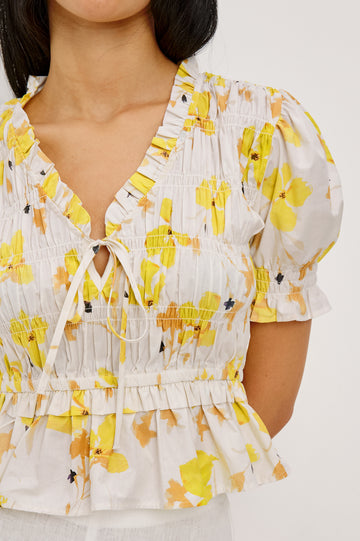 Fontaine Cropped Top in Cotton Poplin With Fitted Smocked Body V-Neckline With Center-Front Ties Short Puff Sleeves Rufle Trim and Peplum Hem in Tossed Daffodils Colorway - Upper Body Close Up Front View Featured on Model