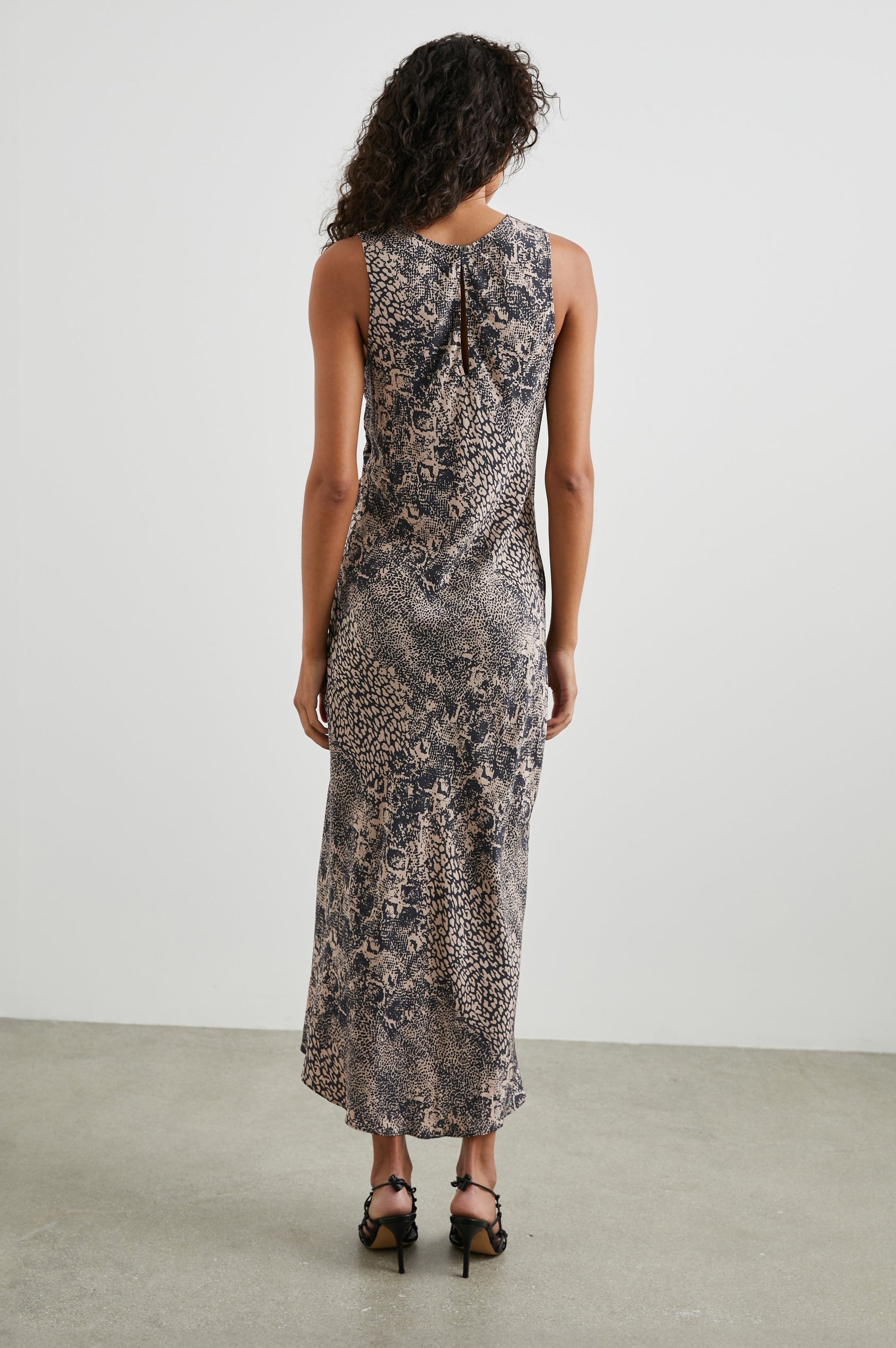 Gabriella Sleeveless Midi Dress with a Crew Neck, a Left Thigh Side Slit, a Ruched Drawstring on the Left Side and a Keyhole Button Closure at the Back in Taupe Mixed Animal Colorway, Mixed Black Spot Patterns on Taupe - Back Full Body View Featured on Model 