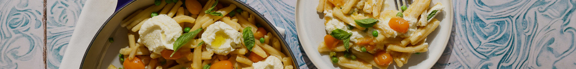 Two plates of pasta with vegetables and cheese on a textured surface