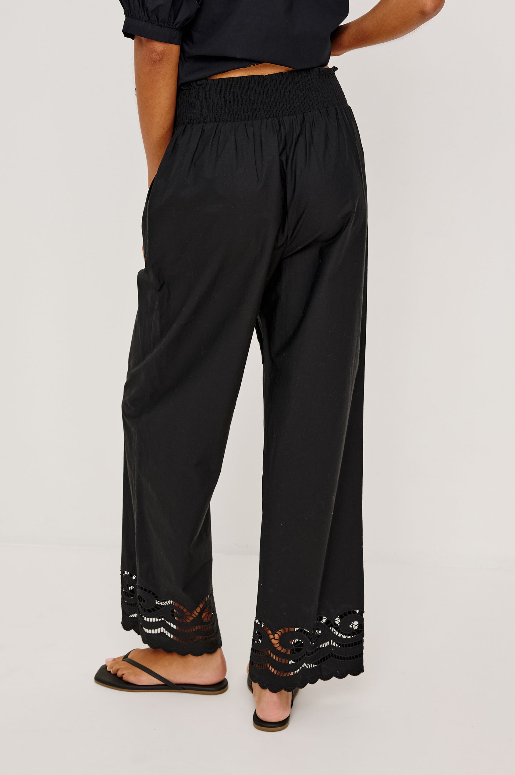 Henrik High-Rise High-Waisted Pant With Wide Smocked Waistband, Side Pockets, Straight Legs, and Scalloped Ladder Embroidered Hem in Black Colorway - Lower Body Back View Featured on Model