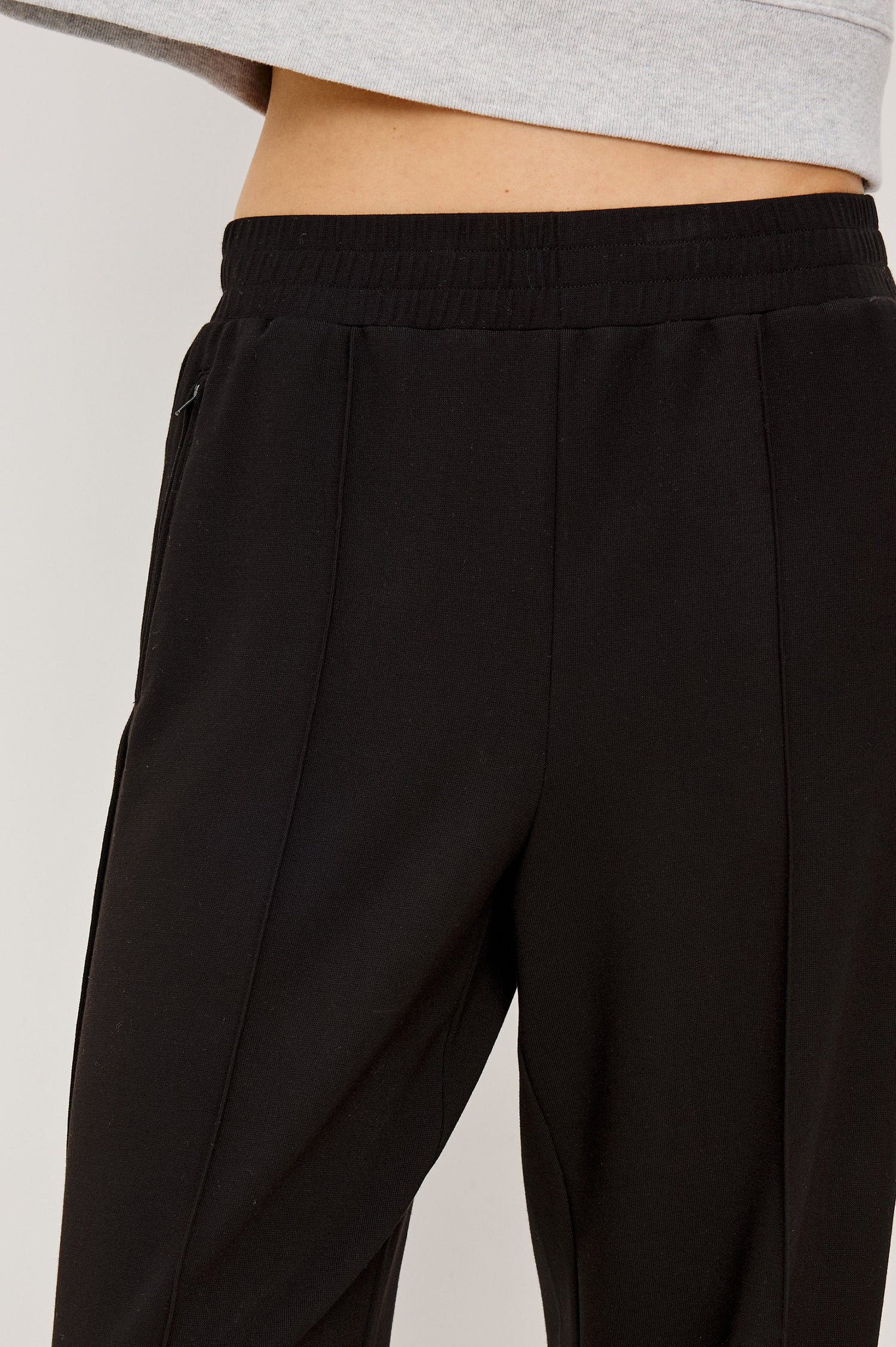 Black ponte pull-on pants with an elastic waistband. The pants feature functional ankle zippers that can be opened to create a subtle flare. Close Up View on Model.