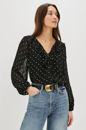 Honora is a lightweight chiffon top with a ruffled neckline and self-tie front closures. The semi-sheer top is partially lined and styled with a soft, feminine silhouette in Polka Dots Colorway - Front View Featured on Model, Shirt Tucked In