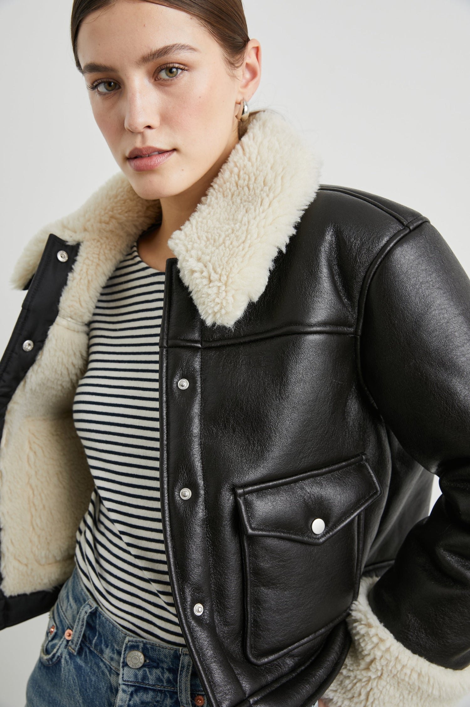 Imani Cropped Faux Leather Jacket with Silver-Toned Snap Closure, Two Front Snap Flap Pockets and Ivory Faux Shearling Lining, Collar and Cuffs in Black Ivory Colorway - Front View Featured on Model  