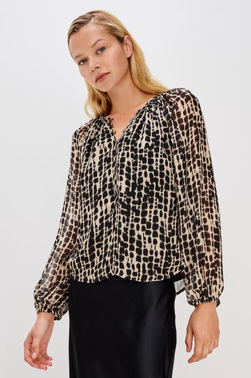 Flowy, 1960s-inspired blouse with a spotted shibori print. The top has sheer, voluminous sleeves with elastic cuffs, natural shell buttons, and a babydoll silhouette. Front View on Model.