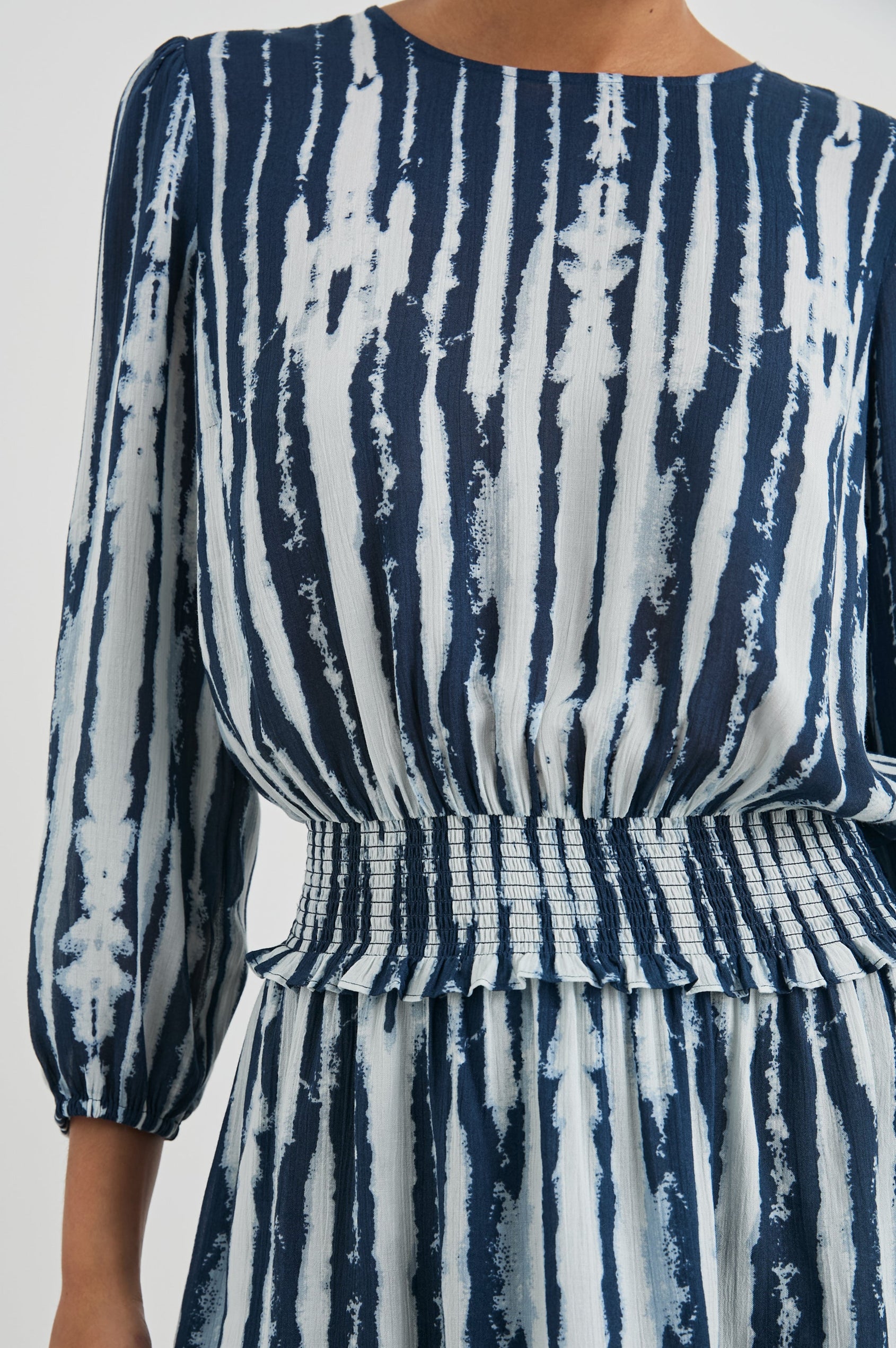 Inez Mini Dress with Three-Quarter Sleeves, a Shallow Scoop Neck, a Smocked Waist, Elasticized Cuffs and a Double Layer Skirt in Indigo Nile Colorway, White and Blue Vertical Streaks - Front View Featured on Model 