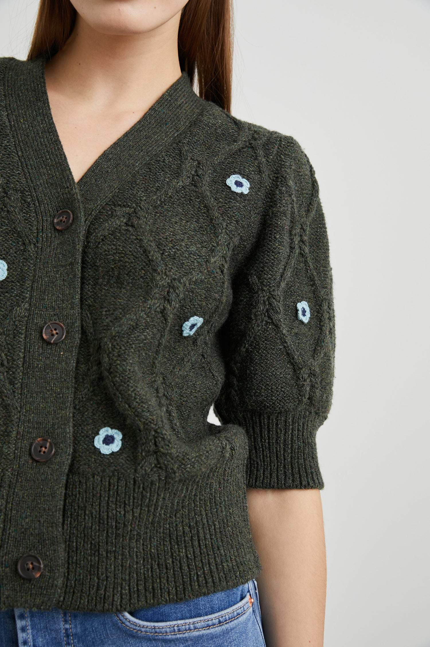 Isla Mid-length-Sleeve Cardigan with Ribbed Hems and Cuffs and Button Closure in Forest Daisies Colorway, with blue crochet daisies on forest green - Front View Featured on Model