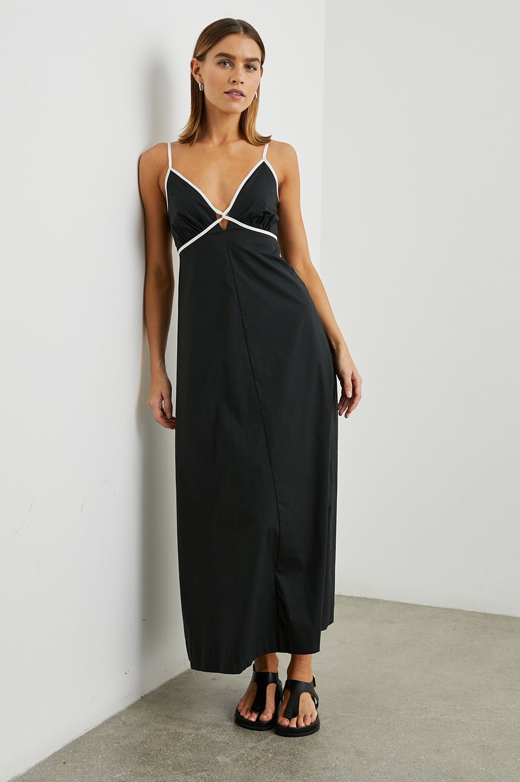 Jessa Sleeveless Maxi Dress with Adjustable Spaghetti Straps, a Deep V Neck with a Cutout, a Shirred Back and White Trim on the Bodice in Black Colorway - Front Full Body View Featured on Model 