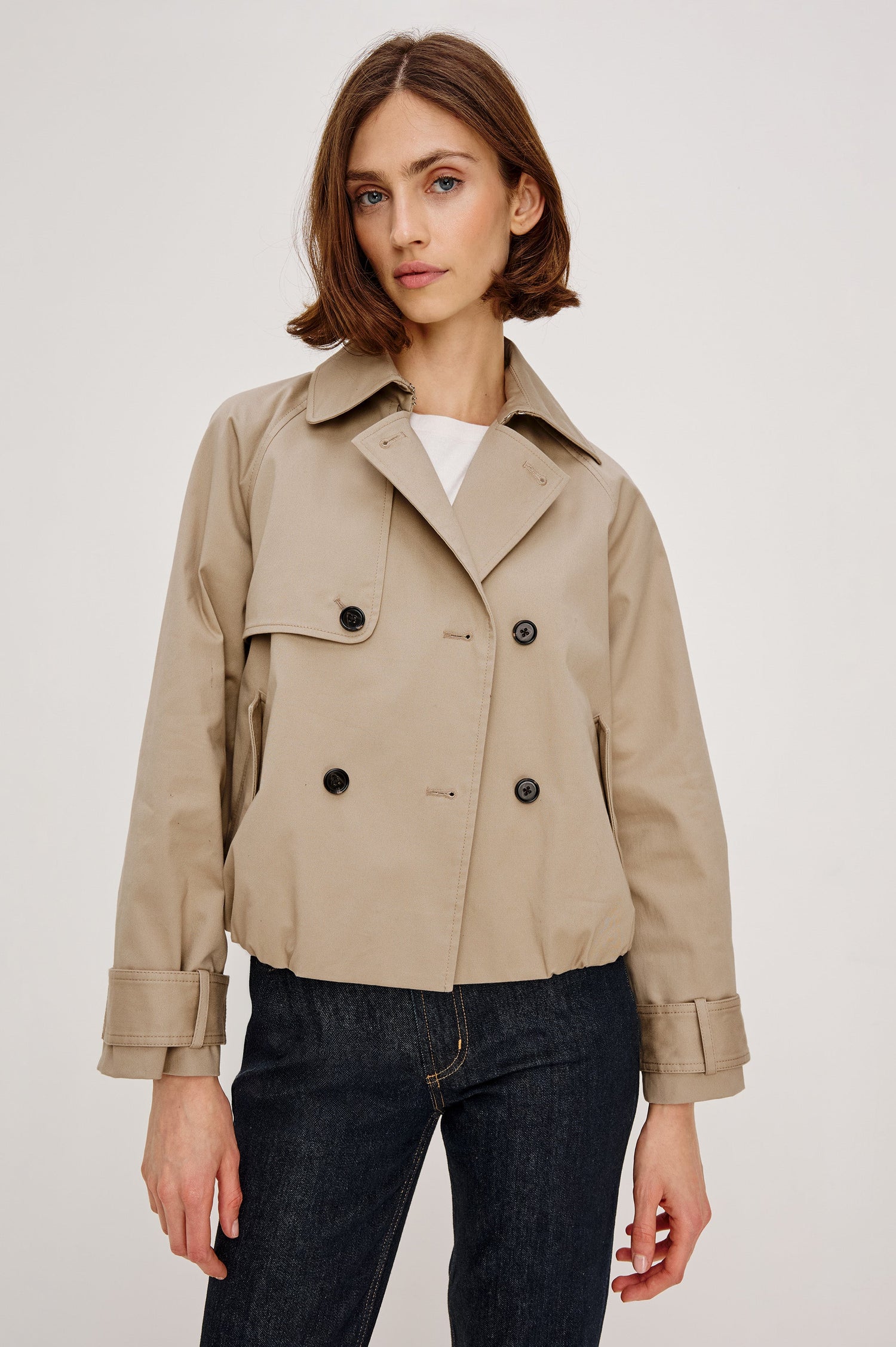 Jett Double Breasted, Cropped Trench Jacket, Lapel, Adjustable Cuff Belt, Side Pockets and Elasticated Hem in Taupe Colorway. Front View Featured on Model.