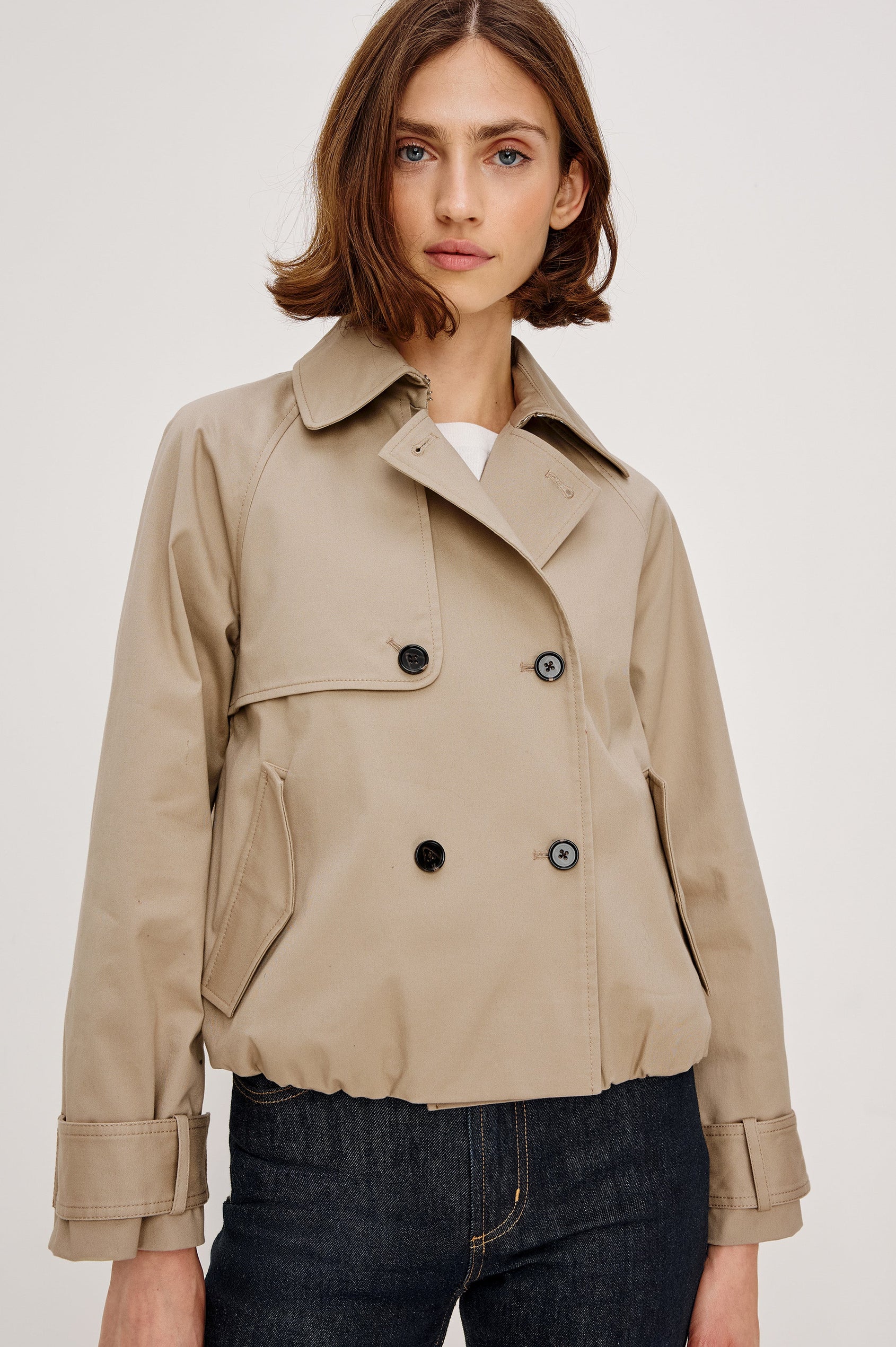 Jett Double Breasted, Cropped Trench Jacket, Lapel, Adjustable Cuff Belt, Side Pockets and Elasticated Hem in Taupe Colorway. Front View Featured on Model.