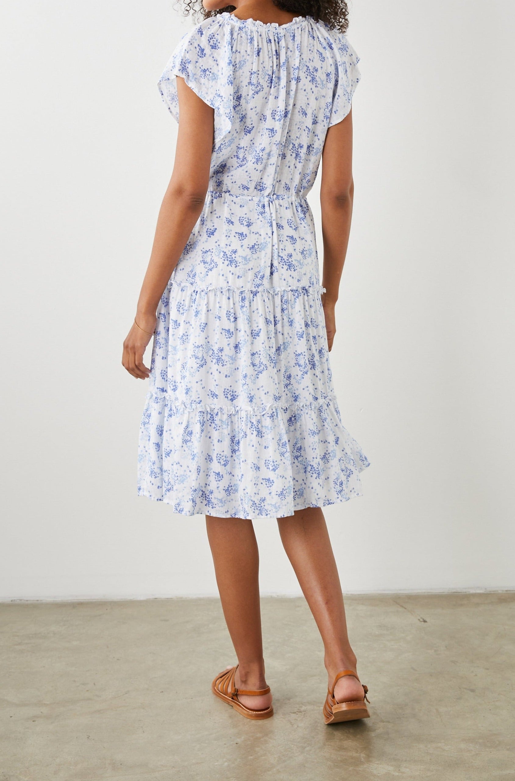 Juni Short Sleeve Midi Dress with a V Neck, Light Ruching along the Neckline, a Drawstring Waist, and a Tiered Skirt in Blue Blossoms Colorway, on White - Back Full Body View Featured on Model