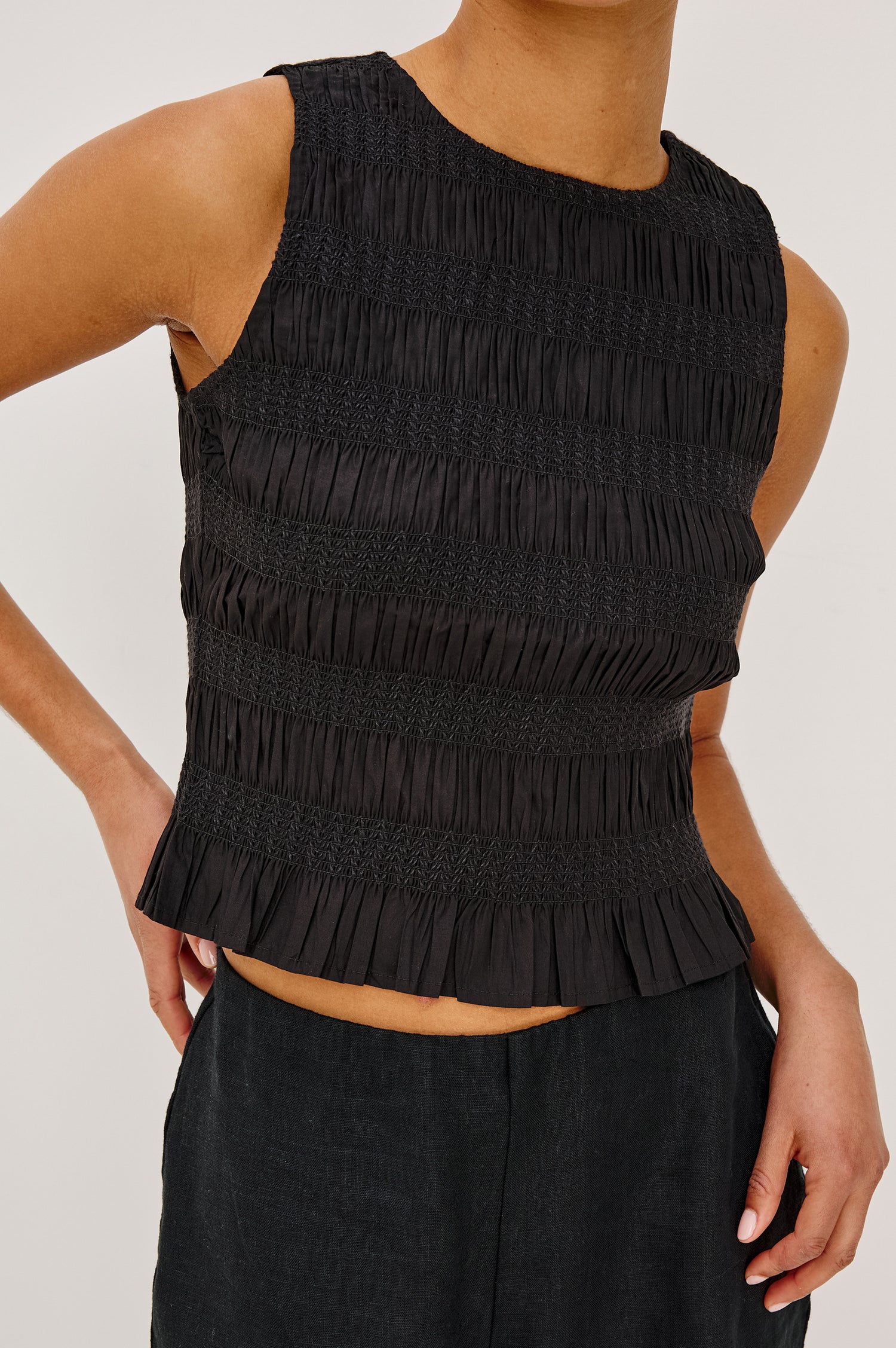 Kane Sleeveless Fitted Top in Cotton With Diamond Smocking All Over, High Boat Neckline, and Flared Ruffle Hem in Black Colorway - Upper Body Close Up Front View Featured on Model