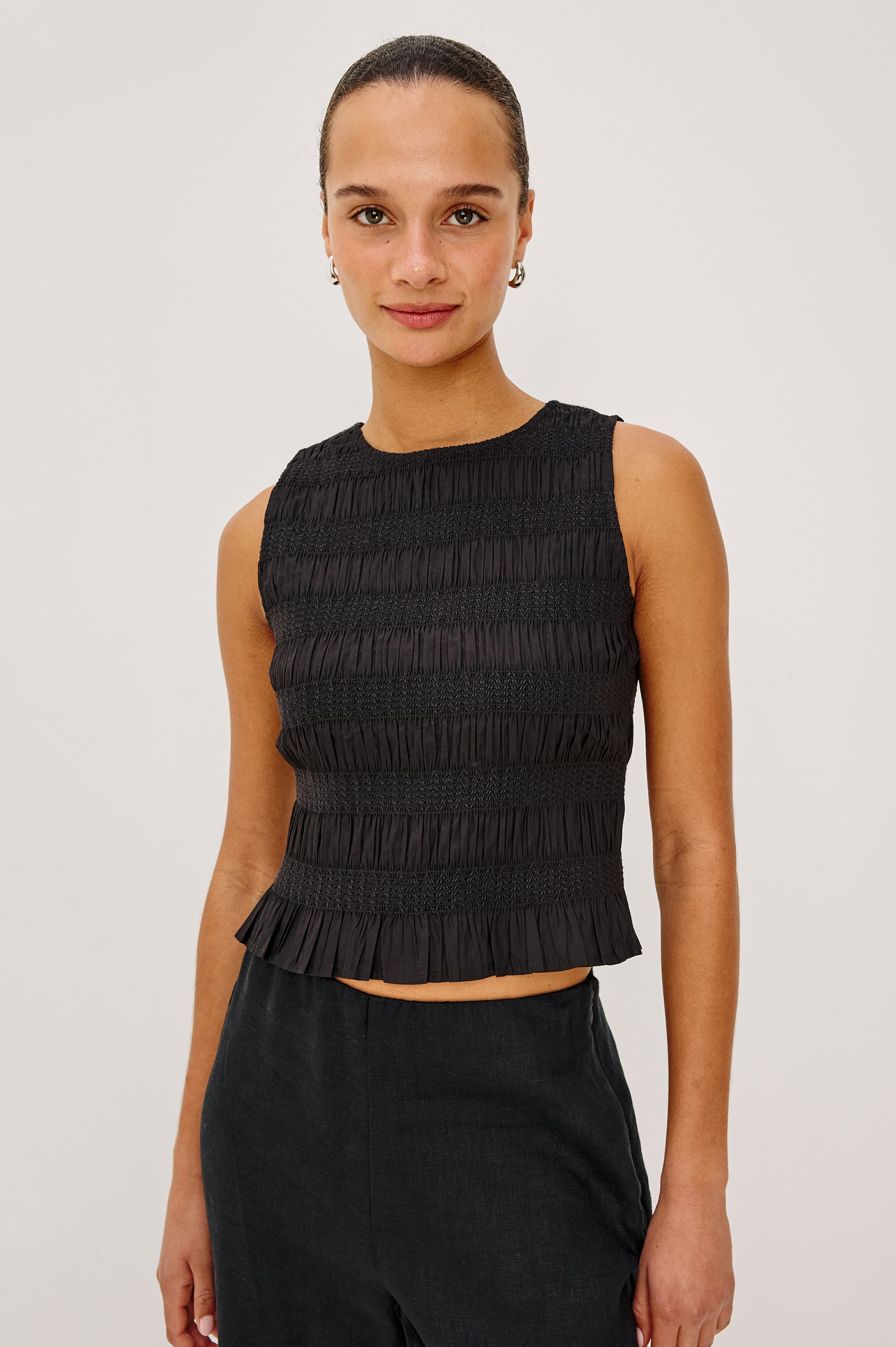 Kane Sleeveless Fitted Top in Cotton With Diamond Smocking All Over, High Boat Neckline, and Flared Ruffle Hem in Black Colorway - Upper Body Front View Featured on Model