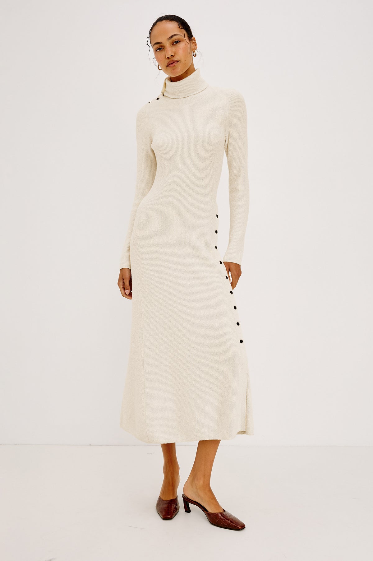 Kat Maxi Dress in Ribbed Cotton Blend With Foldover Turtleneck Button Neckline, Long Sleeves, Fitted Silhouette, Long Sleeves, Side Placket, and Subtle Flare at Hem in Ivory Colorway - Full Body Front View Featured on Model