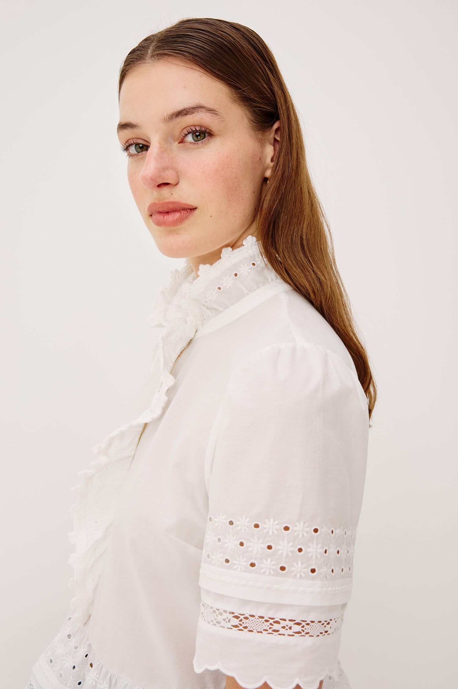 Keeta Shirt in Lightweight Beach Cotton With Ruffled Peter Pan Collar Front Placket Short Sleeves Tiered Hem Crochet Eyelet and Scalloped Trim in White Colorway - Upper Body Side View Featured on Model