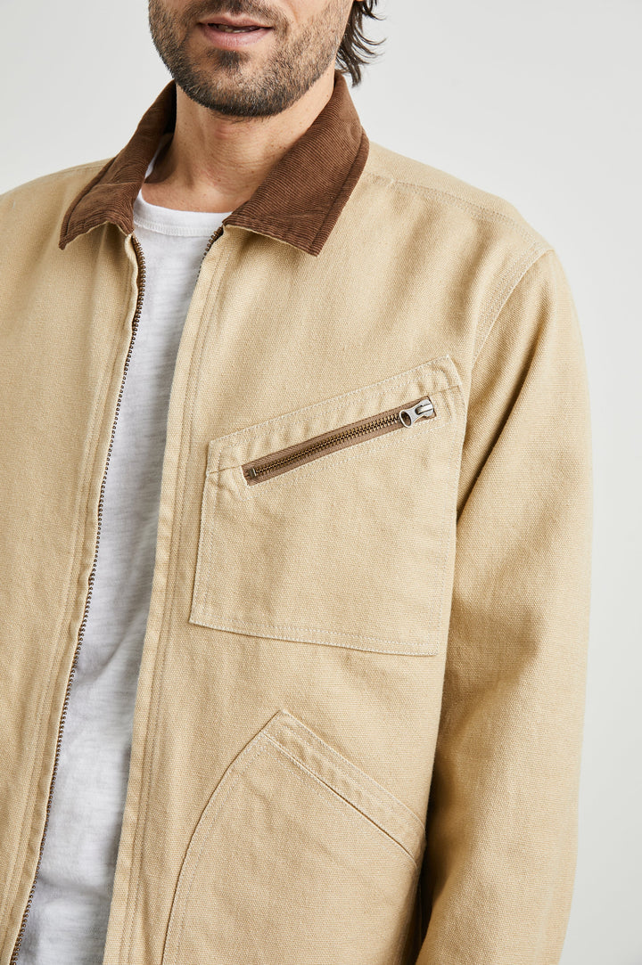 Ketter Zip Up Jacket with Two Curved Front Patch Pockets, a Diagonally Zippered Chest Patch Pocket and Adjustable Button Straps on the Hem in Duck Colorway, a Tan with a Darker Brown Collar - Front View Featured on Model
