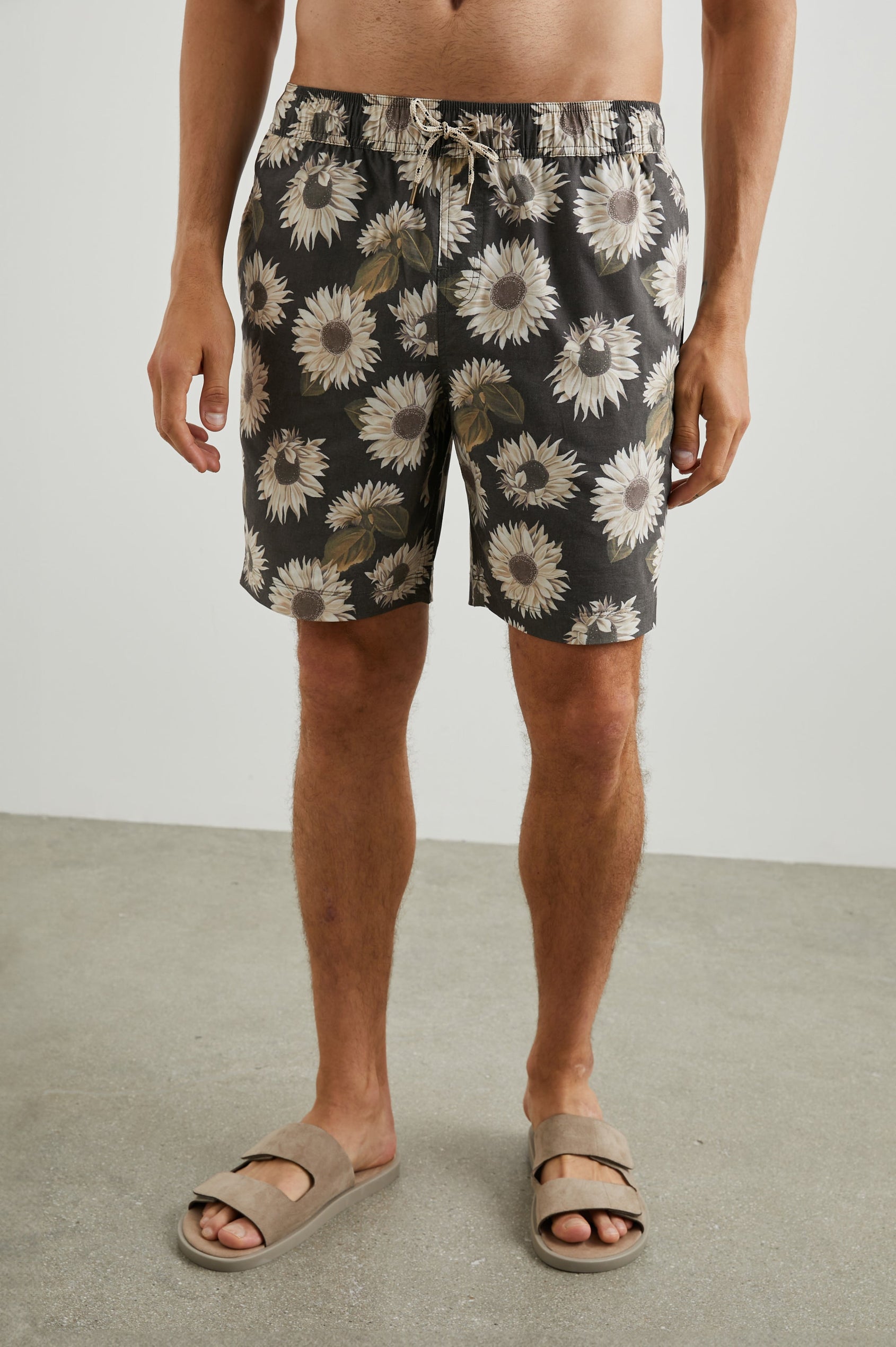 Kian Swim Shorts with an Elastic Drawstring Waistband, Two Front Pockets and a Back Button Flap Pocket in Sunflower Twirl Black Colorway, Sunflowers on Black - Front View Featured on Model